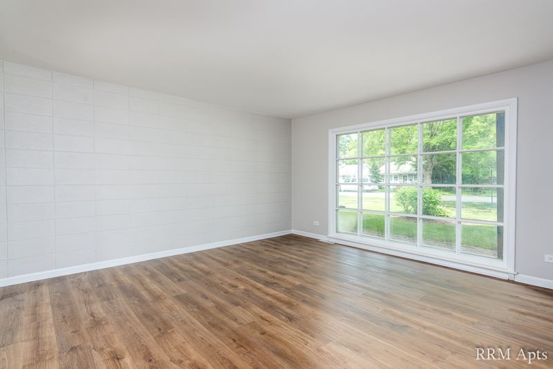 Living room with wood-look floor and a wide picture window overlooking the lawn, South Slusser apartment 434