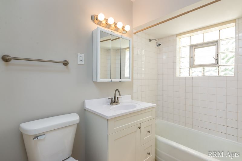 Bathroom with white vanity, mirrored medicine cabinet, tiled tub and glass-block window, South Slusser apartment 434