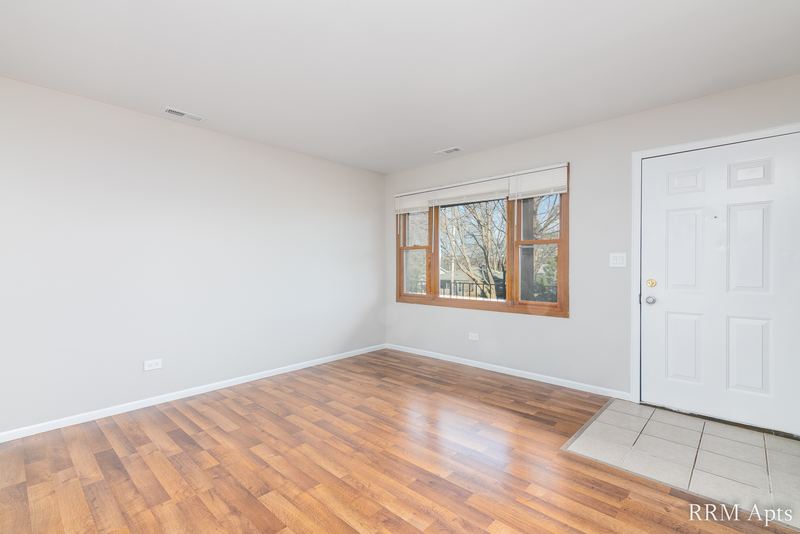 Living room with laminate floor, wood-trimmed window and white entry door with tile entry, South Slusser apartment 440-5