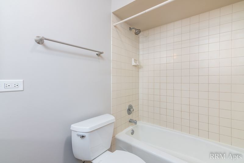 Bathroom with white tile tub surround, white toilet and towel bars, South Slusser apartment 440-5