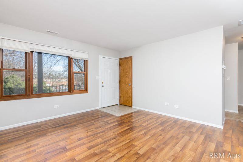 Living room with laminate floor, wide wood-trimmed window, white entry door and wood door, South Slusser apartment 440-5