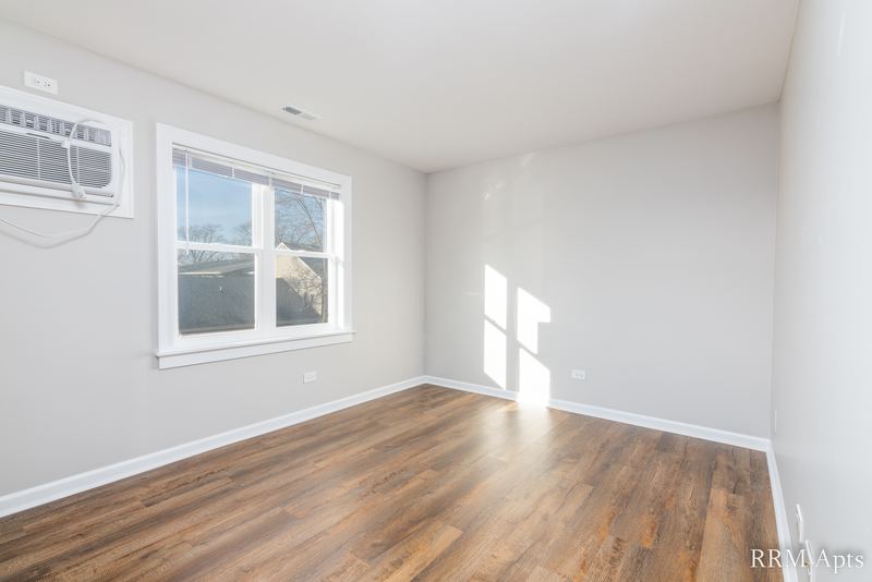Living room with laminate floor, wall air conditioner and wood-trimmed window facing trees, South Slusser apartment 440-5