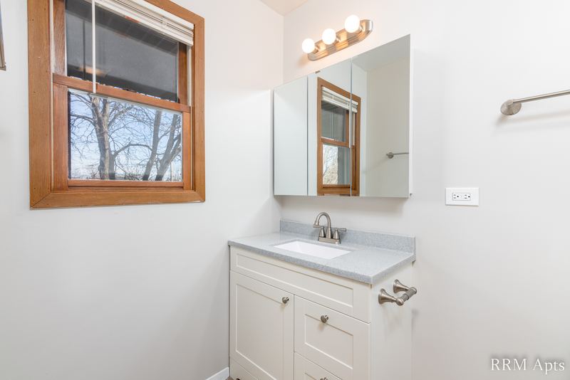 Bathroom with wood-trimmed window, white vanity, mirrored medicine cabinet and vanity light, South Slusser apartment 440-5