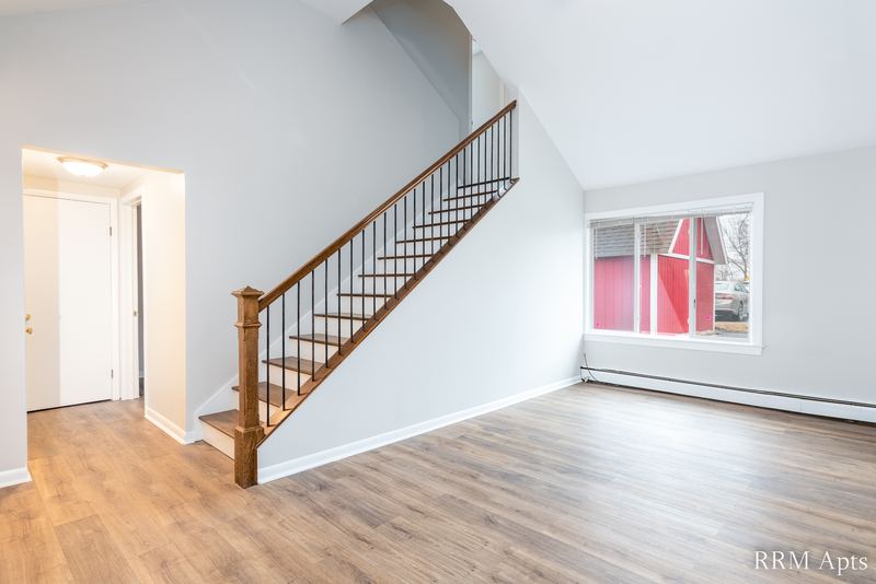 Living room with wood floor, wood-railed staircase, white entry door and window, South Slusser apartment 51 St Paul