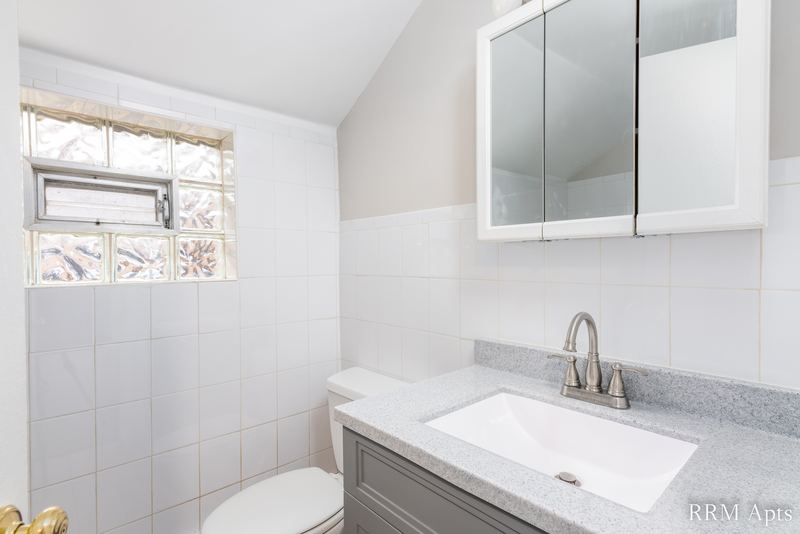 Bathroom with white tile walls, gray vanity, mirrored medicine cabinet and small window, South Slusser apartment 51 St Paul