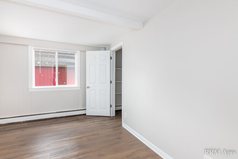 Bedroom with wood floor, window, white door and baseboard radiator, South Slusser apartment 51 St Paul