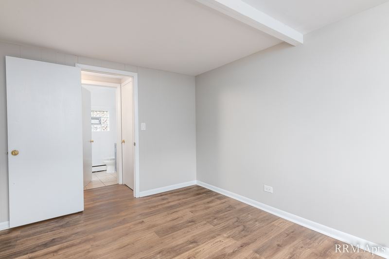 Empty room with wood floor, white door and doorway to the hall with a window at the end, South Slusser apartment 51 St Paul
