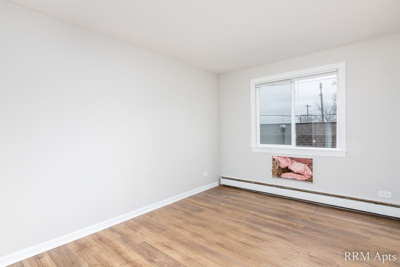 Bedroom with wood floor, window facing a red building and baseboard radiator, South Slusser apartment 51 St Paul