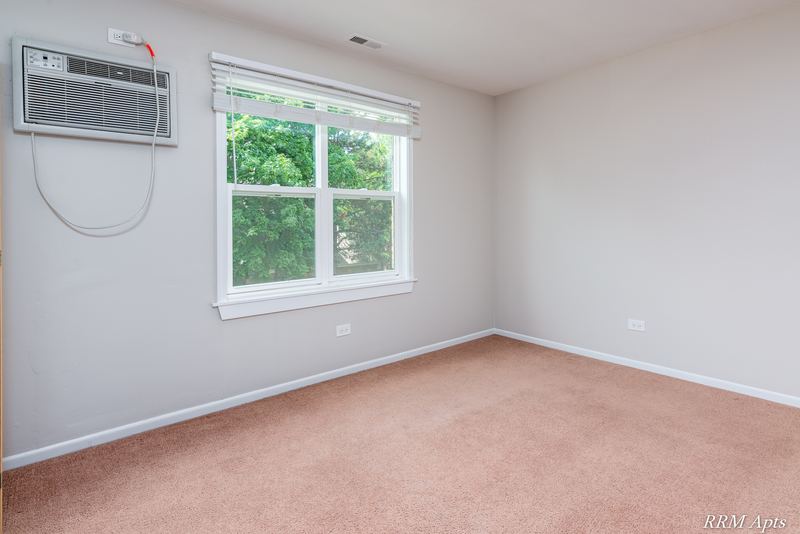 Bedroom with beige carpet, wall air conditioner and window facing trees, South Slusser apartment 440-6