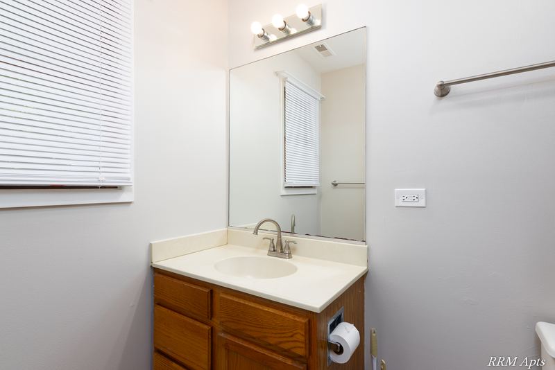 Bathroom with oak vanity, white top, large mirror, vanity light and window with blinds, South Slusser apartment 440-6