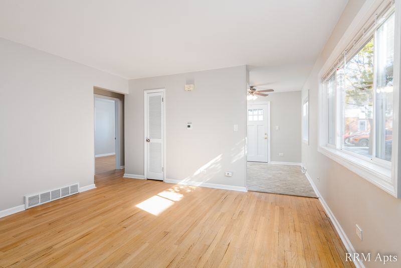 Living room with wood floor, windows along one wall, white doors and kitchen doorway, Westerfield Place apartment 143 B