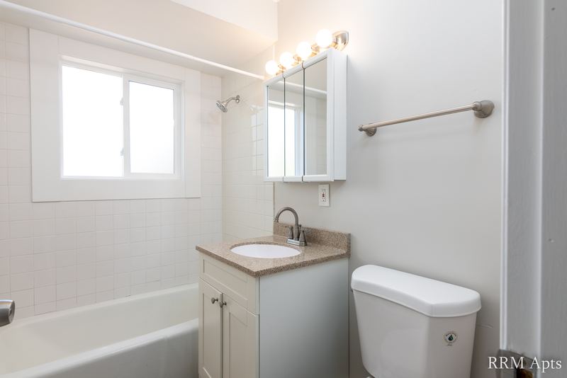 Bathroom with white tile tub surround, window, wood vanity and medicine cabinet, Westerfield Place apartment 143 B