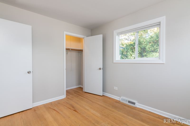 Bedroom with wood floor, open closet with shelf, window facing trees and white door, Westerfield Place apartment 143 B