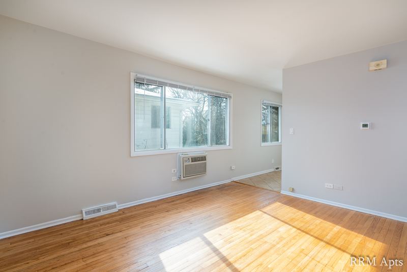 Living room with wood floor, wide window and wall air conditioner beneath it, Westerfield Place apartment 143 C