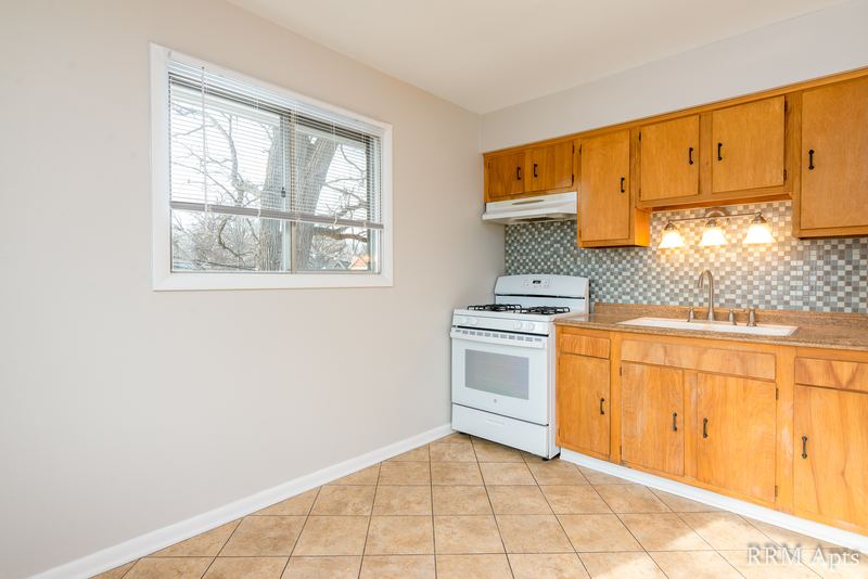 Kitchen with oak cabinets, white gas stove, gray tile backsplash and beige tile floor, Westerfield Place apartment 143 C