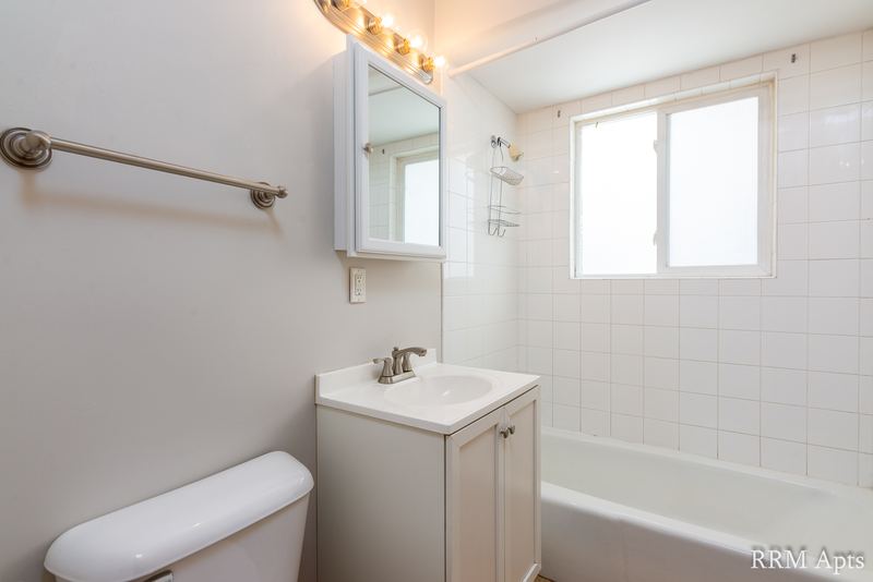 Bathroom with white tile tub surround, window, white vanity and medicine cabinet, Westerfield Place apartment 143 C