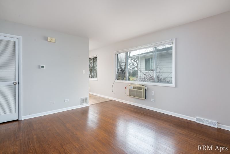 Living room with wood floor, wide window, wall air conditioner and white closet door, Westerfield Place apartment 143 D
