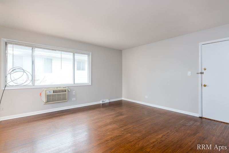Living room with wood floor, window, wall air conditioner and white entry door, Westerfield Place apartment 143 D