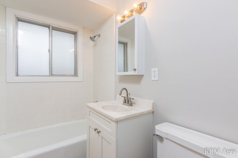 Bathroom with white vanity, window, medicine cabinet, vanity light, white tub and toilet, Westerfield Place apartment 143 D
