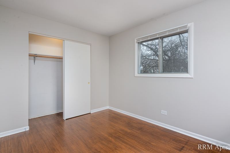 Bedroom with wood floor, open closet with white door and window facing trees, Westerfield Place apartment 143 D