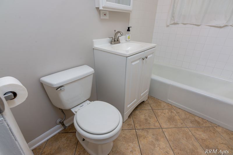 Bathroom with white toilet, white vanity, white tile tub surround and beige tile floor, Westerfield Place apartment 143A