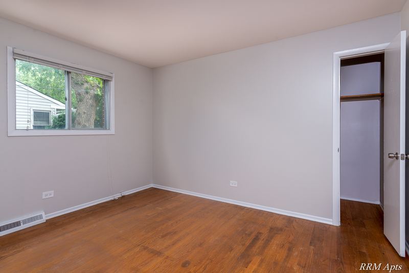 Bedroom with wood floor, window facing trees, white door and open closet with shelf, Westerfield Place apartment 143A