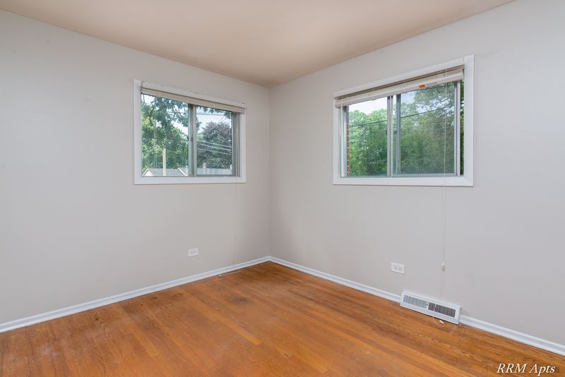 Bedroom with wood floor, two windows facing trees and baseboard radiator, Westerfield Place apartment 143A