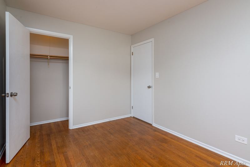 Bedroom with wood floor, white door and open closet with hanging rod and shelf, Westerfield Place apartment 143A
