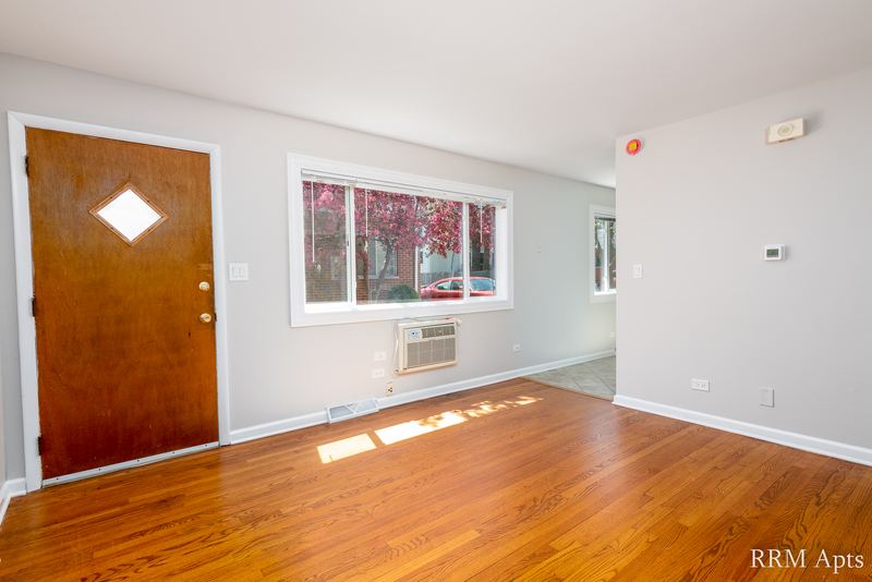Living room with wood floor, wood entry door, window and wall air conditioner, Westerfield Place apartment 145A