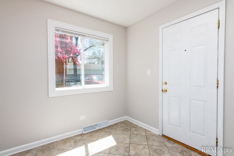 Dining area with beige tile floor, window with blossoming tree outside and white door, Westerfield Place apartment 145A