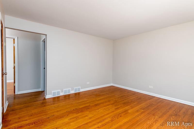 Living room with wood floor, baseboard radiator and open wood door to a bedroom, Westerfield Place apartment 145A