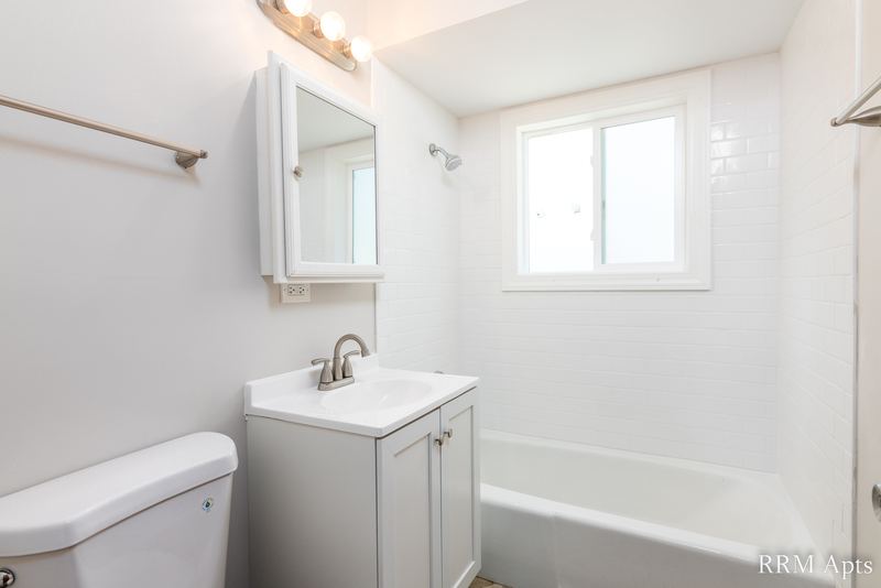 Bathroom with white vanity, medicine cabinet, window and white tile tub surround, Westerfield Place apartment 145A
