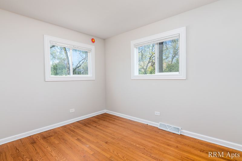 Bedroom with wood floor, gray walls, two windows facing trees and baseboard radiator, Westerfield Place apartment 145A