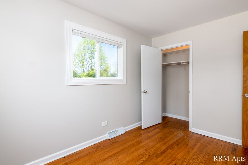Bedroom with wood floor, window facing trees and open closet with white door, Westerfield Place apartment 145A