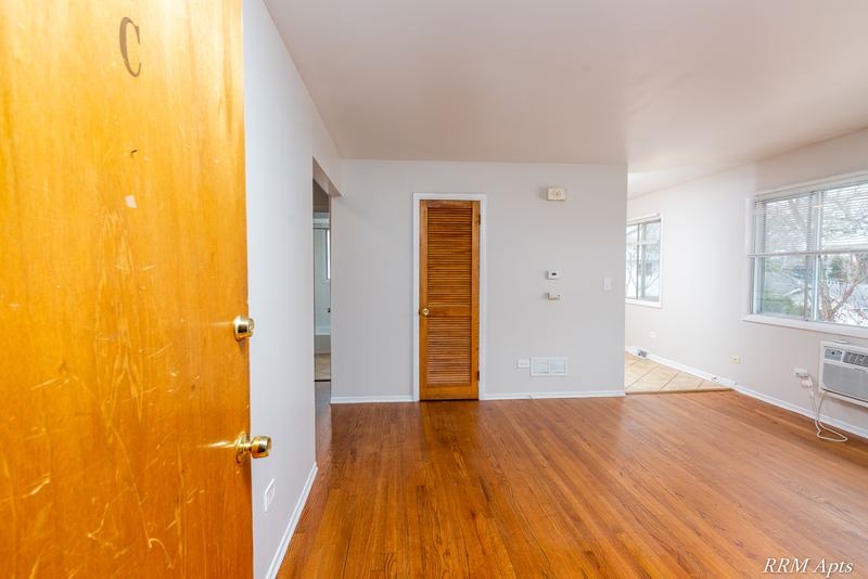 Living room with wood floor, open wood entry door, louvered closet door and window, Westerfield Place apartment 147 C