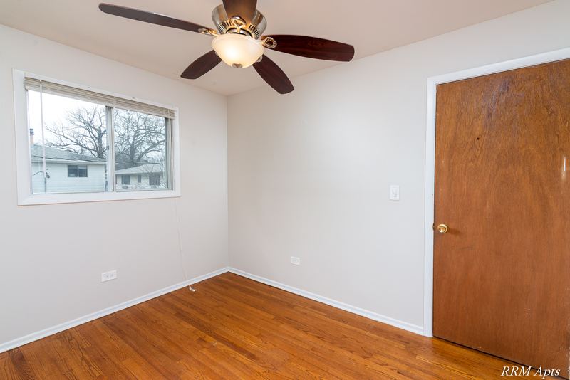 Bedroom with wood floor, ceiling fan, window facing trees and wood door, Westerfield Place apartment 147 C