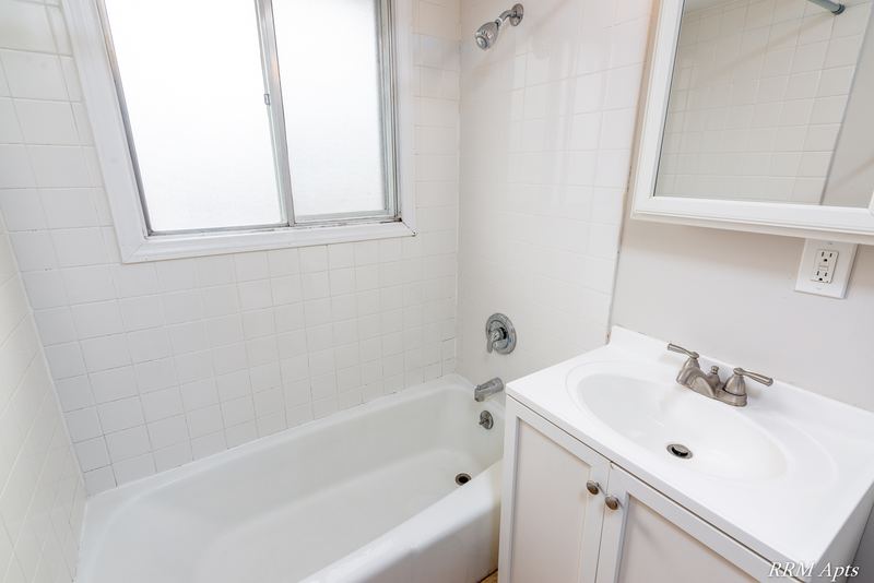 Bathroom with white tile tub surround, window, white vanity and mirror, Westerfield Place apartment 147 C