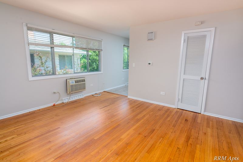 Living room with wood floor, wide window, wall air conditioner and white louvered door, Westerfield Place apartment 147 D