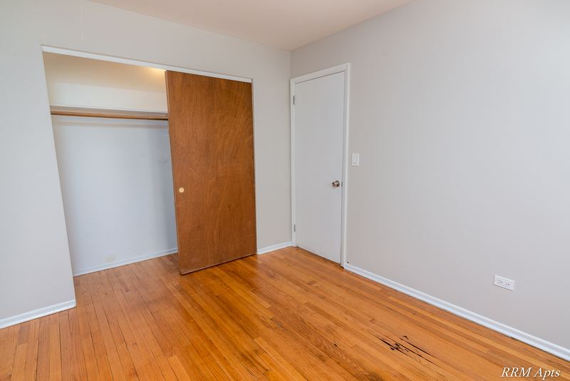 Bedroom with wood floor, open closet with wood sliding door and white entry door, Westerfield Place apartment 147 D