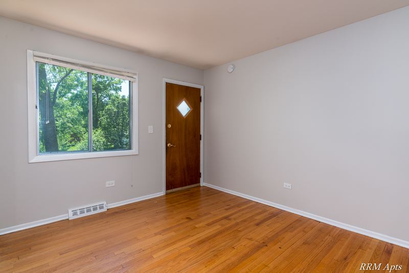 Living room with wood floor, window, baseboard radiator and wood entry door, Westerfield Place apartment 147 D