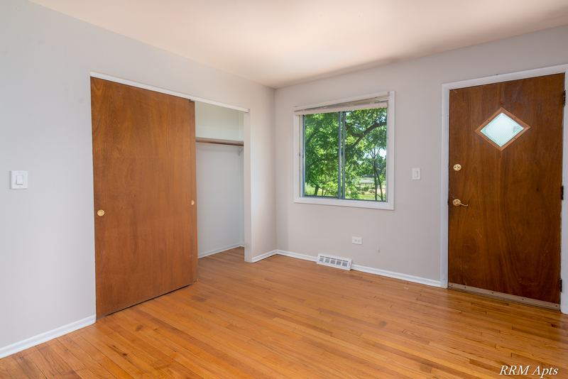 Living room with wood floor, open wood door, window and entry door with diamond window, Westerfield Place apartment 147 D
