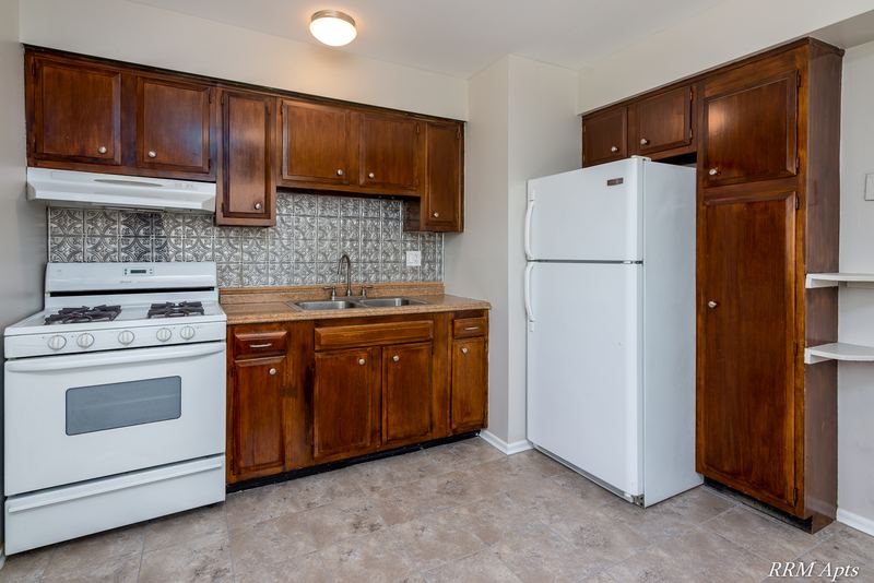Kitchen with dark wood cabinets, white gas stove, refrigerator and beige tile floor, Westerfield Place apartment 147 D