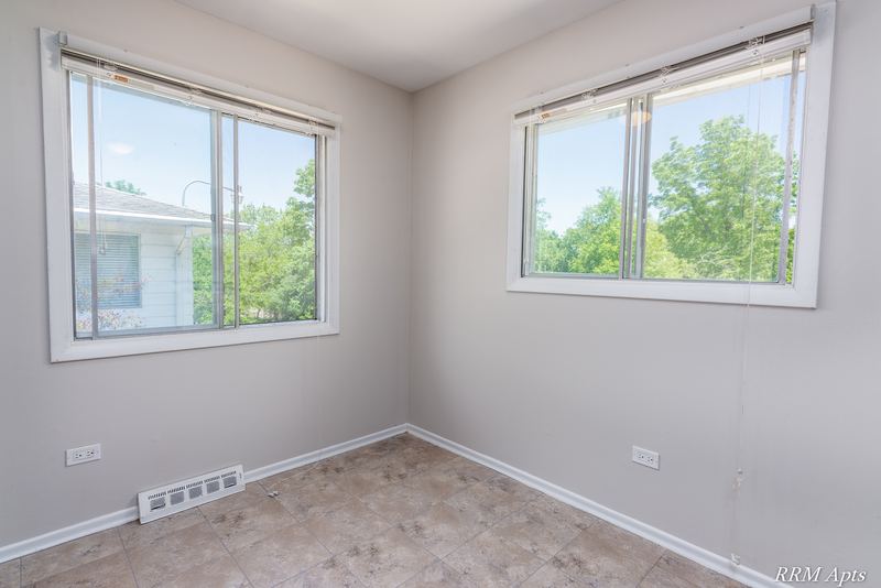 Dining area with beige tile floor, baseboard radiator and two windows facing trees, Westerfield Place apartment 147 D