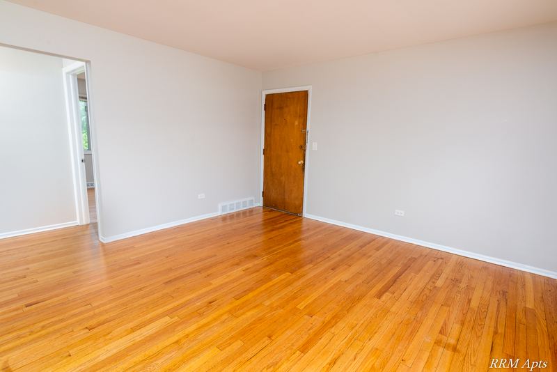 Living room with wood floor, wood door, doorway to the kitchen and baseboard radiator, Westerfield Place apartment 147 D