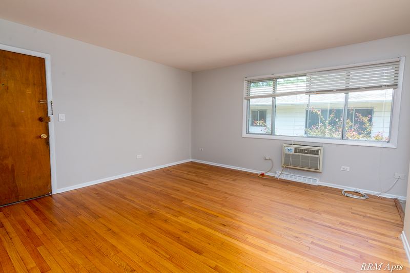 Living room with wood floor, wood entry door, wide window and wall air conditioner, Westerfield Place apartment 147 D