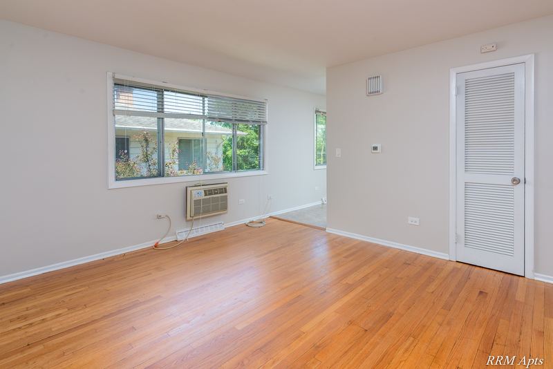 Living room with wood floor, wall air conditioner under the window and louvered door, Westerfield Place apartment 147 D