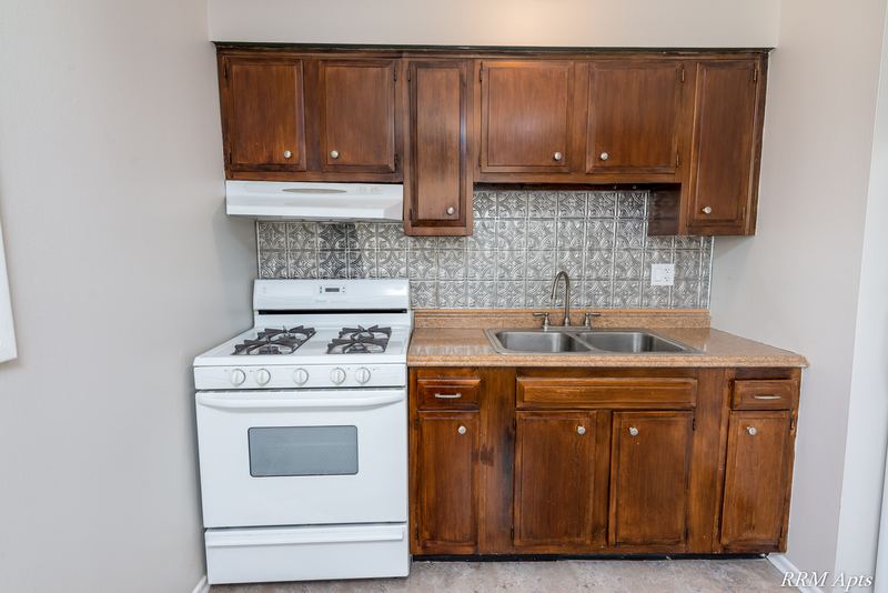Kitchen with dark wood cabinets, white gas stove, range hood and gray tile backsplash, Westerfield Place apartment 147 D