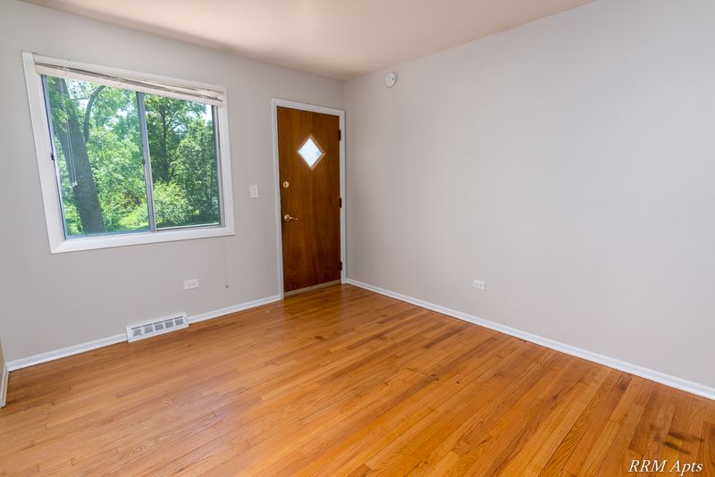 Living room with wood floor, window facing trees and wood entry door with diamond window, Westerfield Place apartment 147 D
