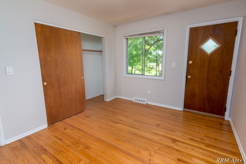 Living room with wood floor, open wood closet, window and wood door with diamond window, Westerfield Place apartment 147 D