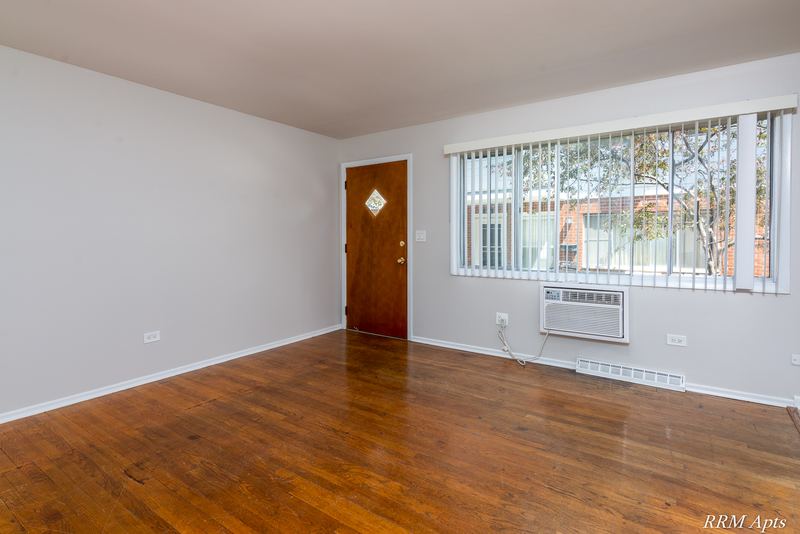 Living room with wood floor, wood entry door, window with blinds and wall air conditioner, Westerfield Place apartment 147B